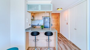 A modern kitchen with a granite countertop, two bar stools, a refrigerator, and wooden cabinets. - Rincon Miramar (Concón)
