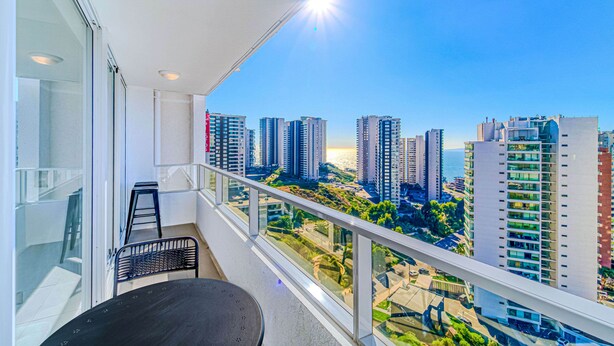 A balcony with a table and chairs, overlooking a cityscape with high-rise buildings and a clear sky. - Rincon Miramar (Concón)