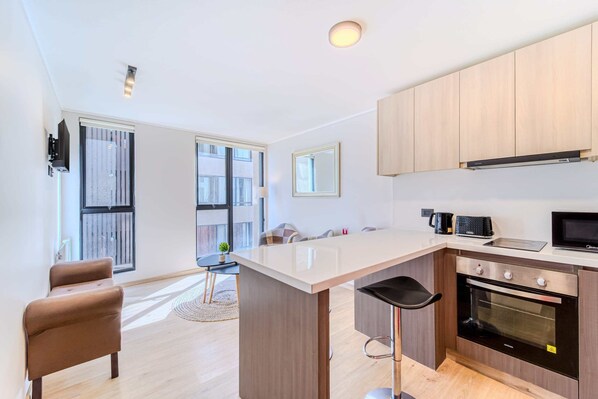 A modern kitchen with a large island, built-in oven, microwave, and wooden cabinets.