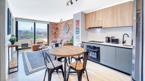A modern kitchen with a city view, a dining area with a round table, and a living space with a sofa and a plant. - Espacio Nunoa 1BR, balcony and free parking (Ñuñoa)