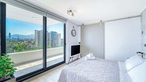 A modern hotel room with a large balcony, a bed, a TV, and a wall-mounted clock. - Espacio Nunoa 1BR, balcony and free parking (Ñuñoa)