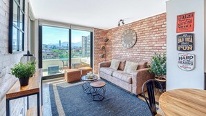 A modern living room with a brick wall, a large window, a sofa, a coffee table, and a dining table. - Espacio Nunoa 1BR, balcony and free parking (Ñuñoa)