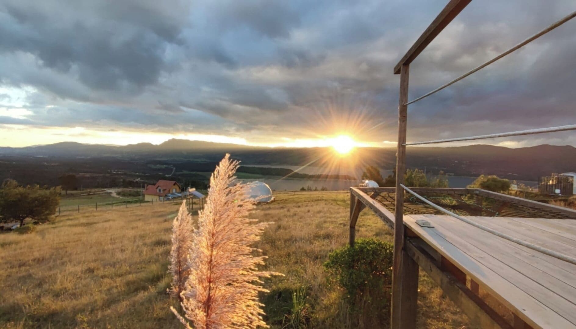 A wooden deck overlooking a grassy field with a sunset in the background.