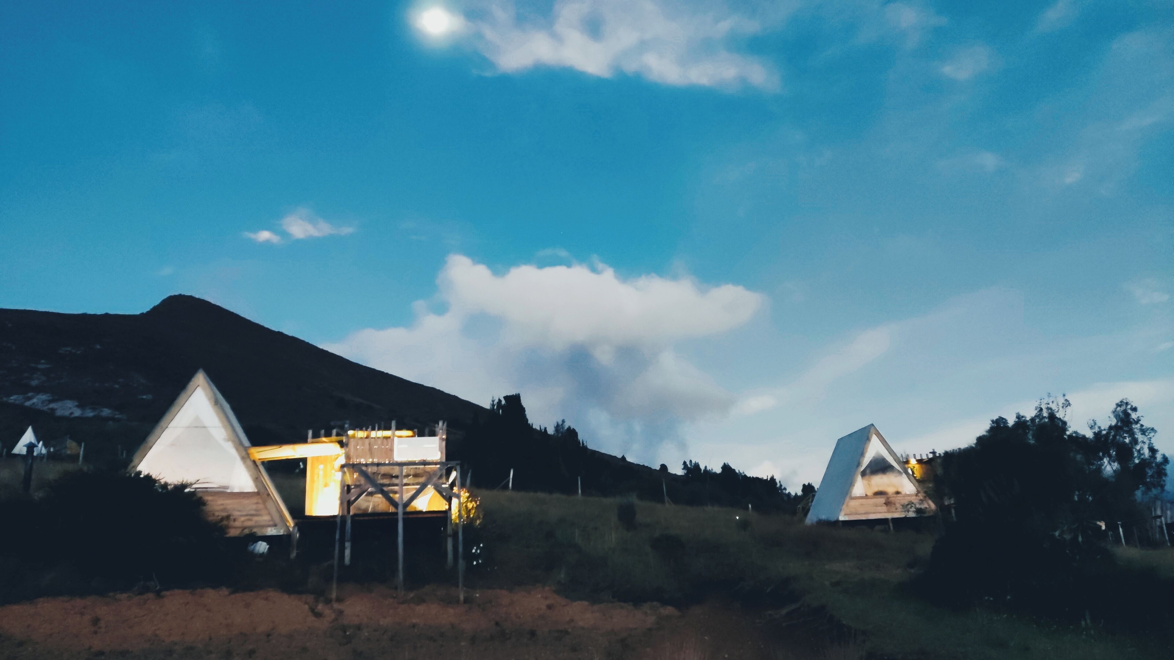 A campsite with tents and a small building, surrounded by a mountainous landscape.