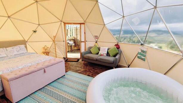 Una stanza a cupola geodetica con un letto, un divano, una vasca idromassaggio e vista sul paesaggio.