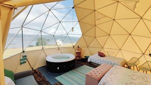 Una tenda a cupola geodetica con vasca idromassaggio, un letto e una zona relax.