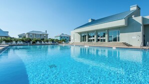 Una piscina con agua azul cristalina, rodeada de sillas de descanso y un edificio con amplios ventanales.