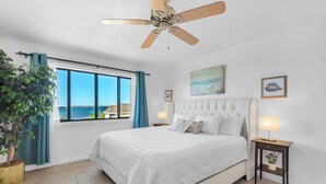 A bedroom with a large bed, a ceiling fan, a window with a view of the sea, and a potted plant. - 🏝️Sound Views | Walk to Beach☀️ Santa Rosa Dunes 722 (Pensacola Beach)