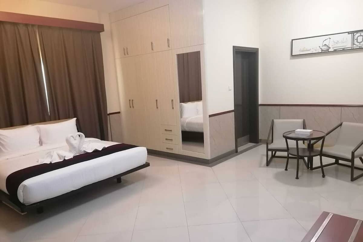 A hotel room with a bed, a wardrobe, a small table with chairs, and a painting on the wall.