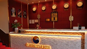 A hotel reception desk with clocks displaying Moscow, London, and New Delhi times, a reception desk with a logo, and a red carpeted area. - Claridge Star Hotel (Ras Al Khaimah)