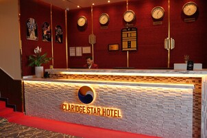 Un mostrador de recepción de hotel con relojes que marcan la hora de Moscú, Londres y Nueva Delhi, un mostrador con un logotipo y una zona alfombrada de color rojo.