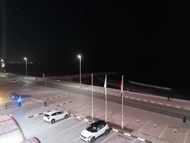 Un estacionamiento nocturno con varios coches, farolas y banderas.