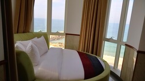 A bed with a view of the beach and ocean through large windows. - Claridge Star Hotel (Ras Al Khaimah)