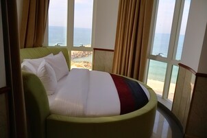 Una cama con vista a la playa y al océano a través de amplias ventanas.