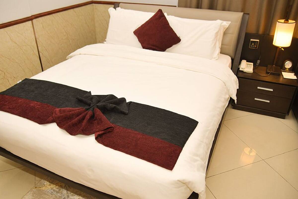 A neatly made bed with a white and red bedspread, a single red pillow, and a bedside table with a lamp and a phone.