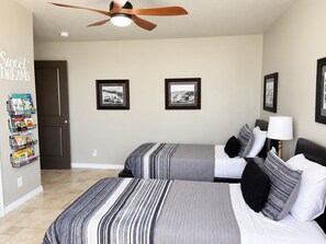 A hotel room with two beds, a ceiling fan, and framed pictures on the wall.