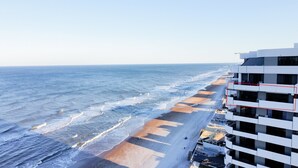 A coastal hotel with a beach view, featuring a modern architectural design with balconies and a clear view of the ocean. - Oceanfront Condo Wraparound Balcony Sunrise Views (Daytona Beach)