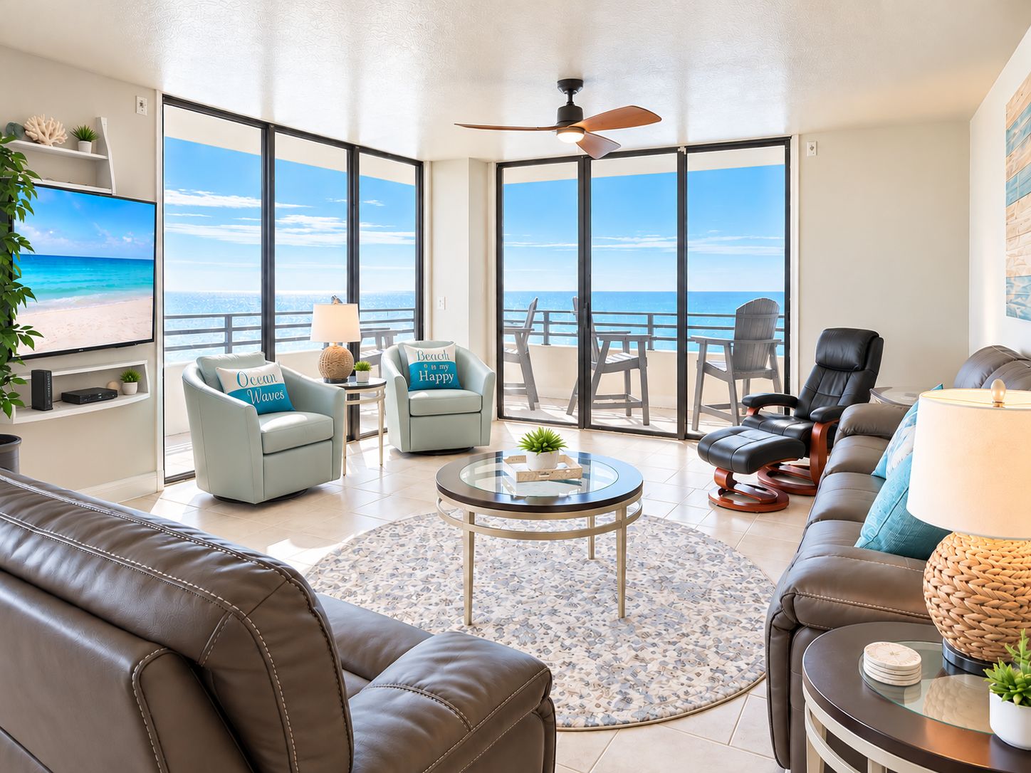 A spacious living area with a large TV, comfortable seating, a ceiling fan, and a view of the ocean.