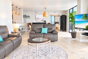 A modern living room with a leather sofa, a glass coffee table, and a flat-screen TV. - Oceanfront Condo Wraparound Balcony Sunrise Views (Daytona Beach)