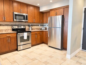 A modern kitchen with wooden cabinets, stainless steel appliances, and a tiled floor.