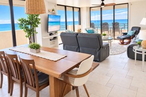 A modern living room with a wooden dining table, grey sofas, and a view of the ocean. - Oceanfront Condo Wraparound Balcony Sunrise Views (Daytona Beach)