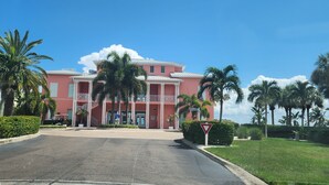A pink building with a white roof, surrounded by palm trees and a clear blue sky.