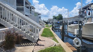 A canal with boats docked on the right, a white staircase leading down to the water, and a grassy area with a pathway.