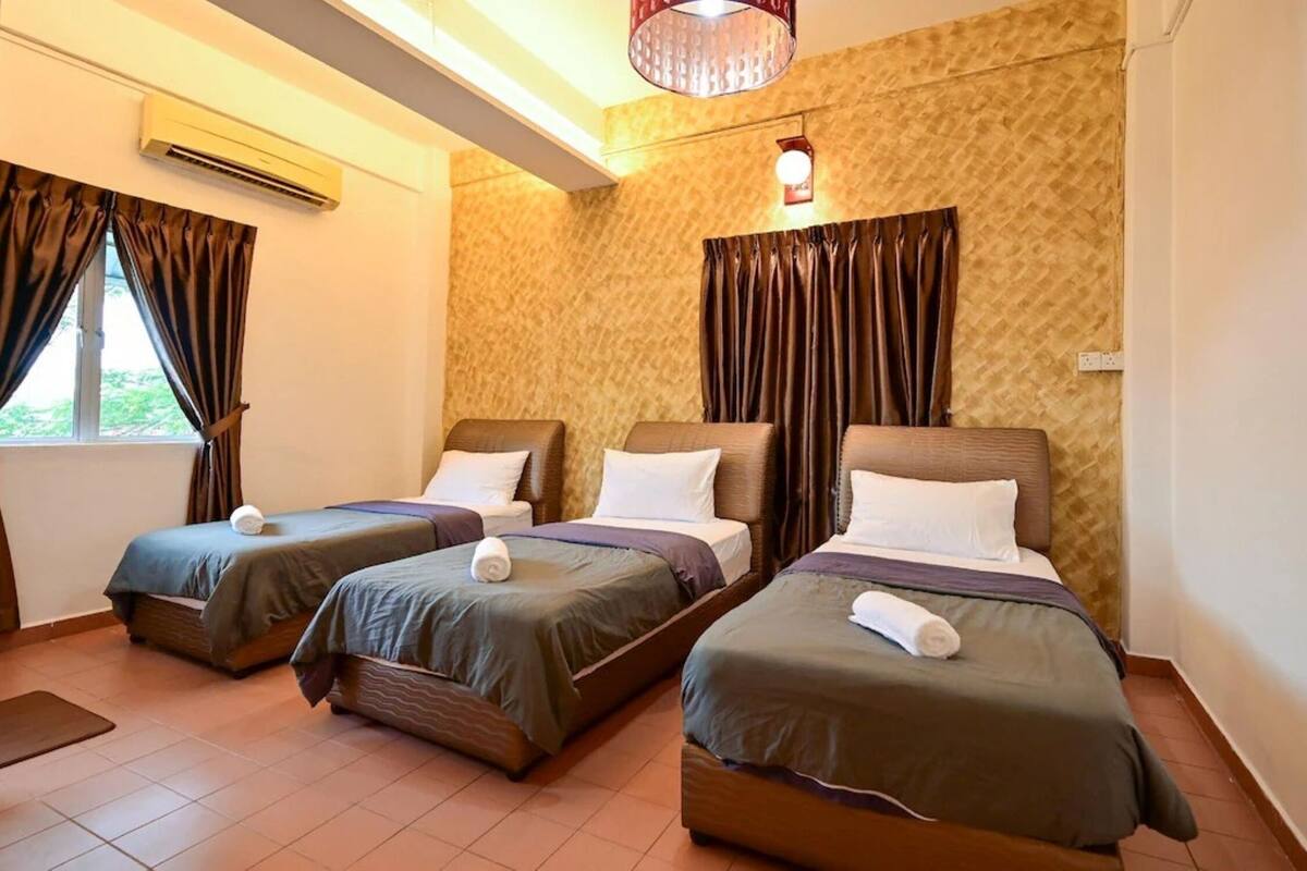 Une chambre d’hôtel avec trois lits simples, une fenêtre avec des rideaux, un appareil de climatisation et un mur décoré d’un motif.