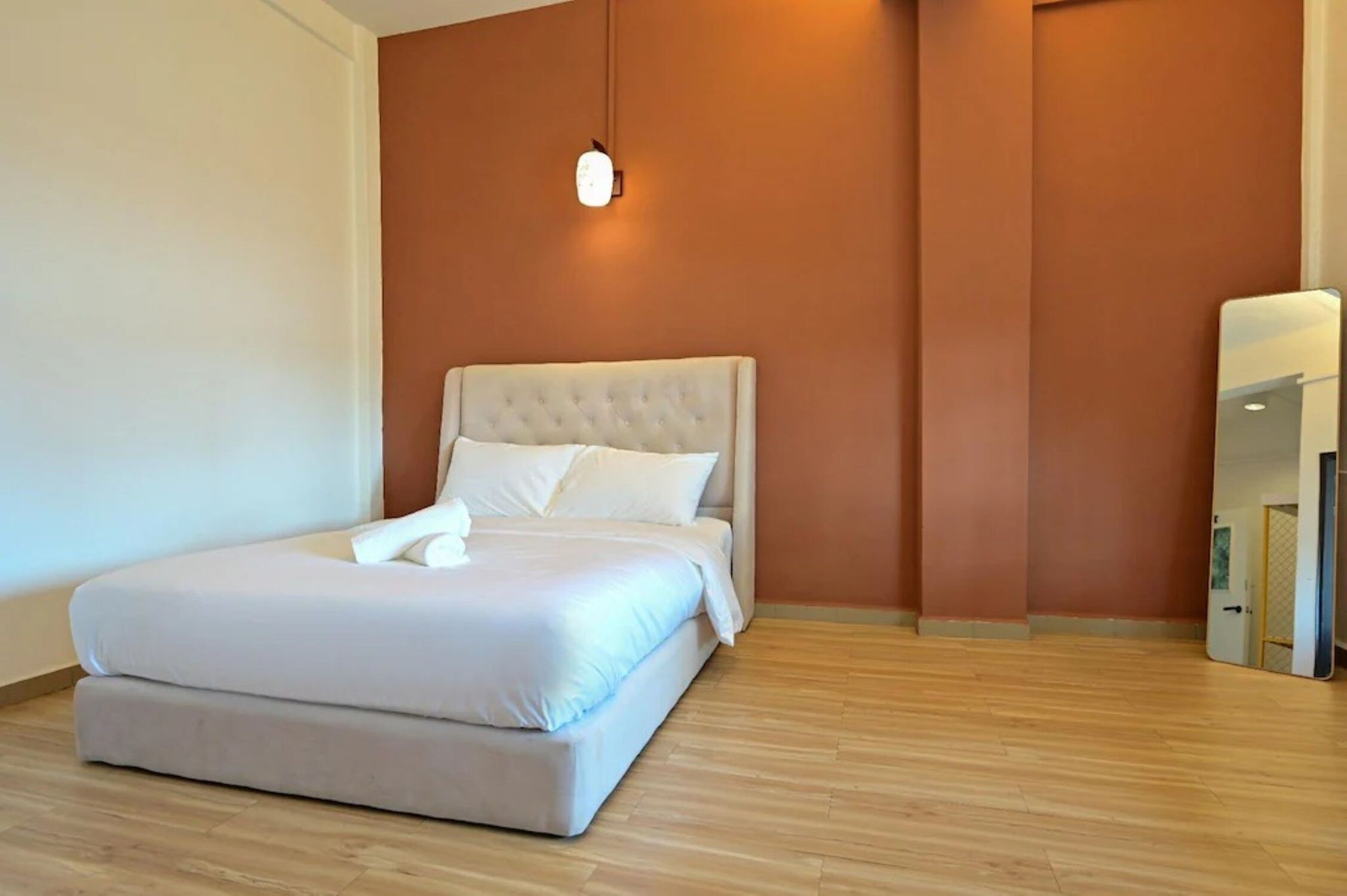 A neatly made bed in a room with wooden flooring and a brown accent wall.
