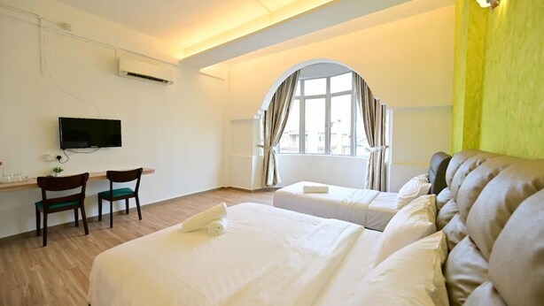 A hotel room with two beds, a desk with chairs, a TV, and a window with curtains. - First Star Homestay (Kluang)