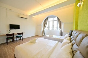A hotel room with two beds, a desk with chairs, a TV, and a window with curtains.