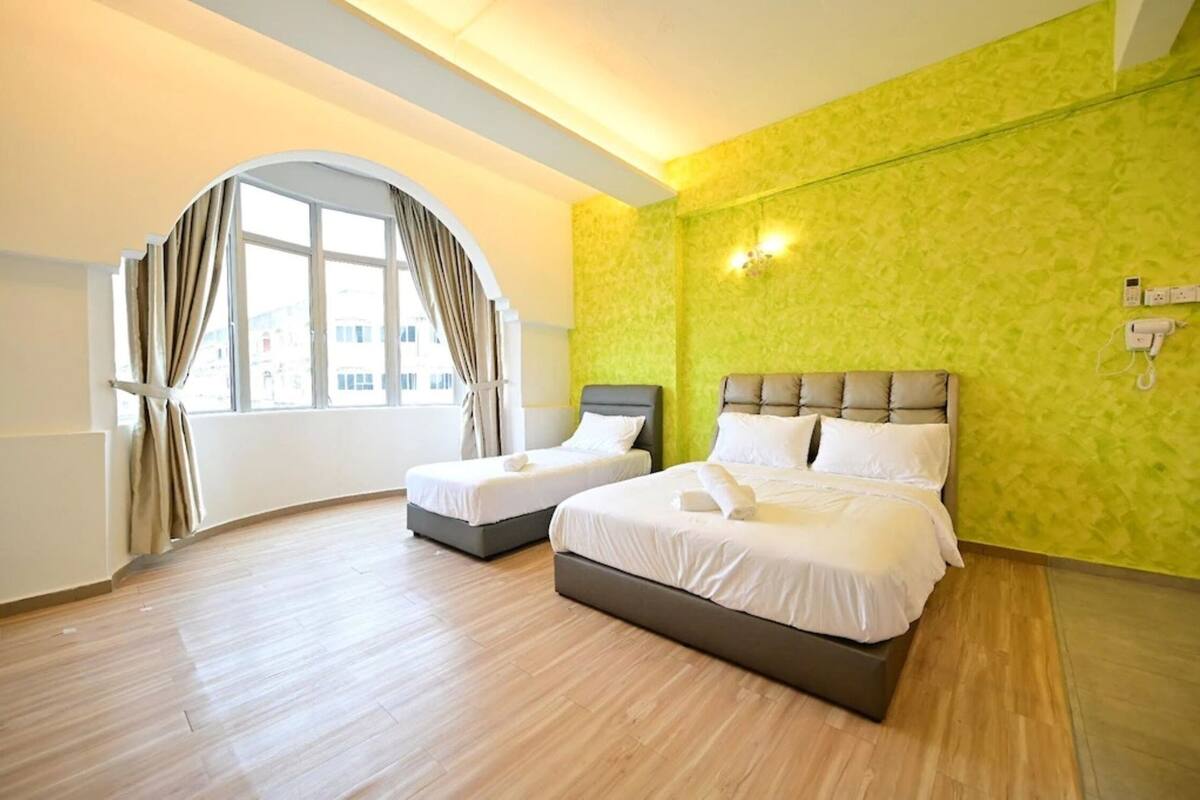 Une chambre d’hôtel avec deux lits, une grande fenêtre avec des rideaux et un mur vert à texture.