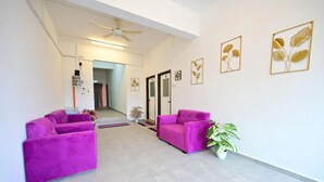 A spacious living area with two purple sofas, a ceiling fan, and framed botanical artwork on the walls. - First Star Homestay (Kluang)