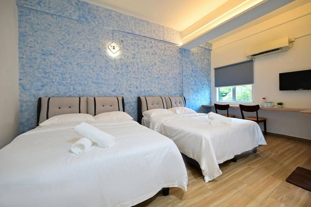 Une chambre d’hôtel avec deux lits, un téléviseur fixé au mur et une fenêtre donnant sur un paysage verdoyant.