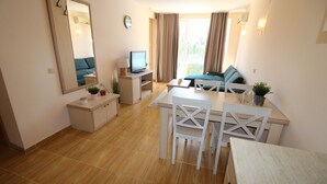 A modern living room with a dining area, a television, a sofa, and a large window with curtains. - Menada Paradise Dreams Apartments (Sveti Vlas)