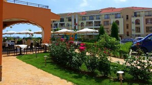 An outdoor patio area with tables and chairs, surrounded by greenery and flowers. - Menada Paradise Dreams Apartments (Sveti Vlas)