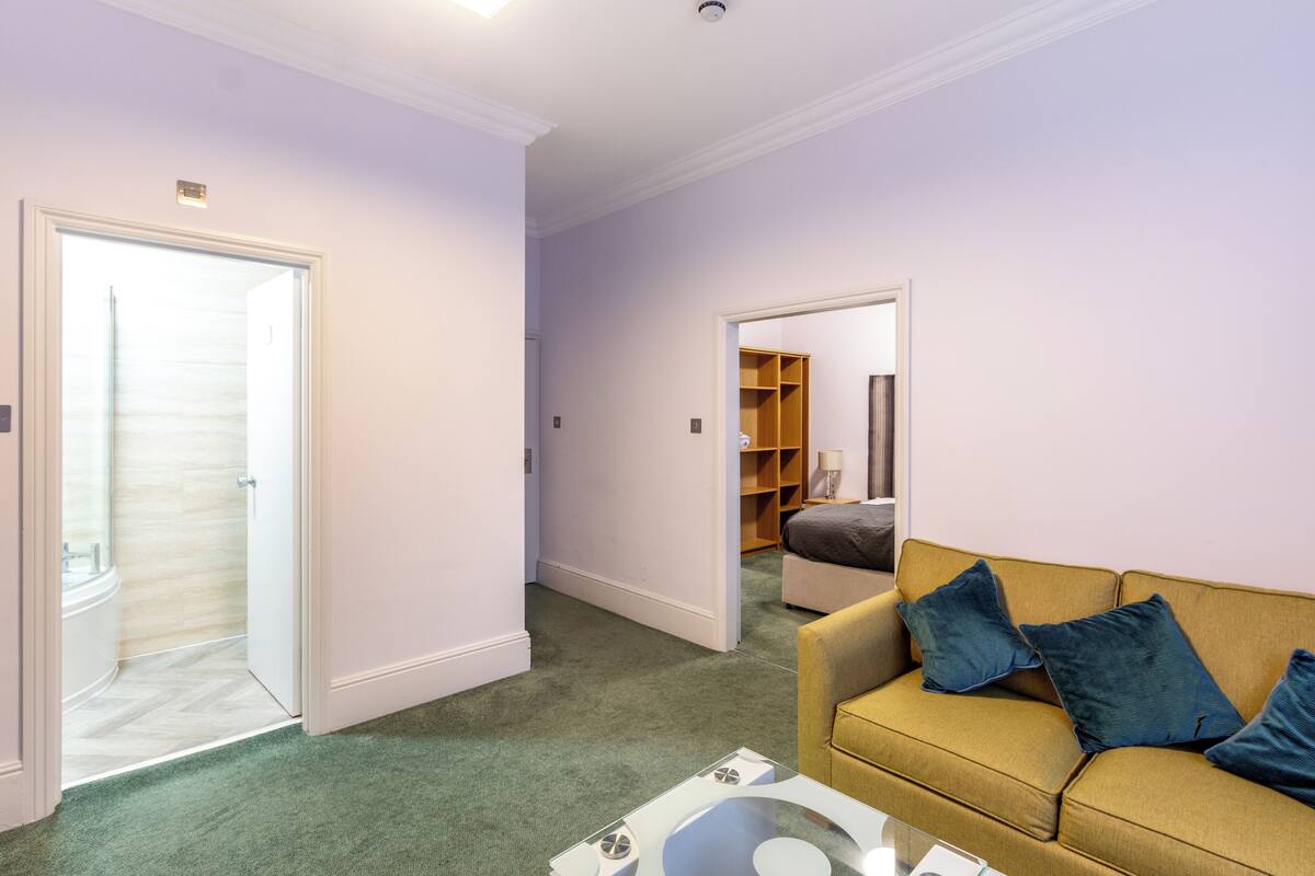 A living room with a yellow sofa, a coffee table, and a door leading to a bathroom.