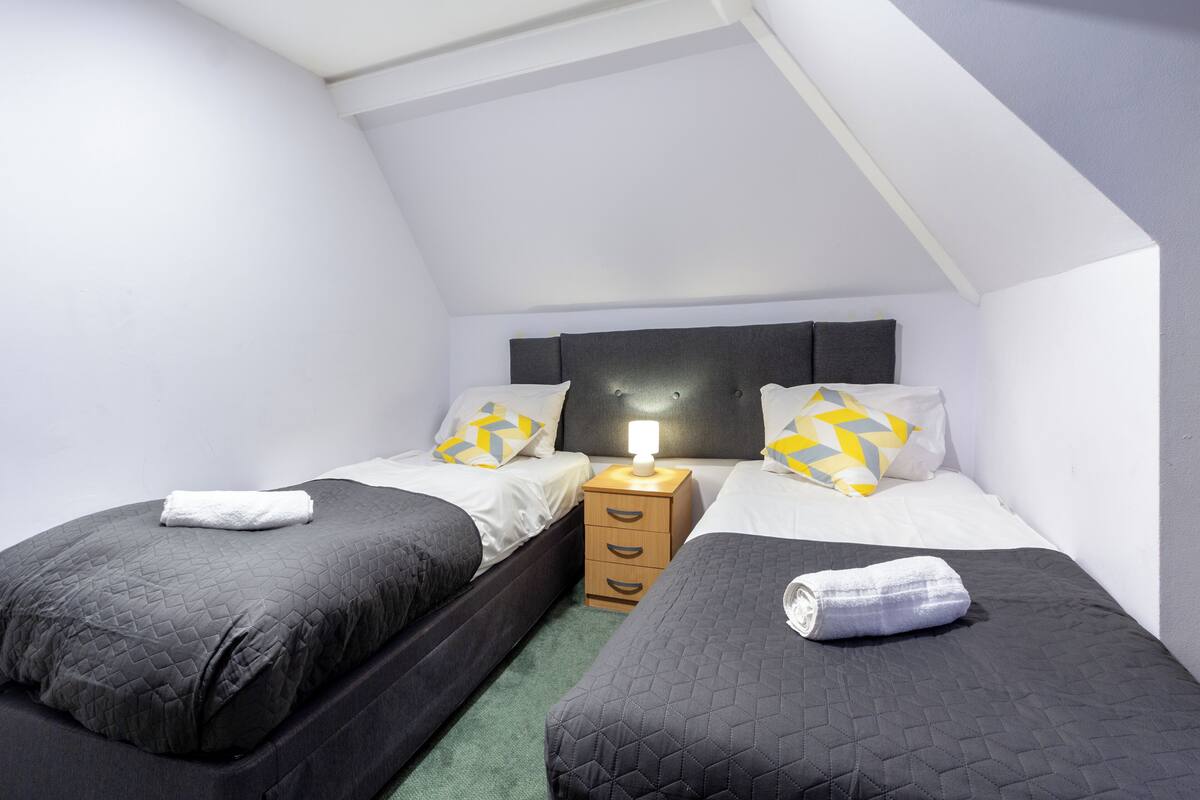 A room with two beds, a nightstand with a lamp, and a wooden drawer unit.