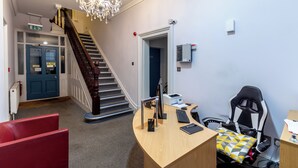 A modern office space with a desk, computer, and gaming chair. A staircase with a chandelier is visible in the background. - London Gatwick Inn (Horley)