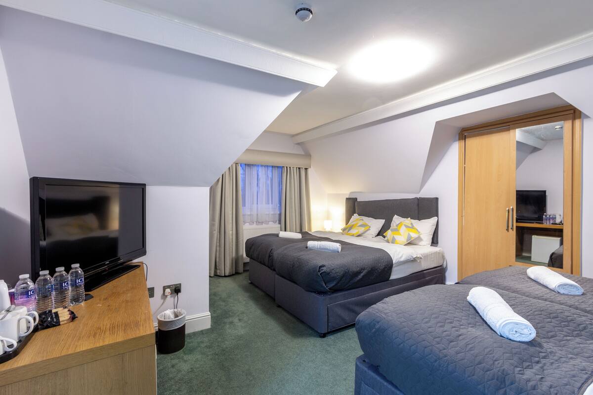 A hotel room with a flat-screen TV, two beds, a wooden dresser, and a TV stand.