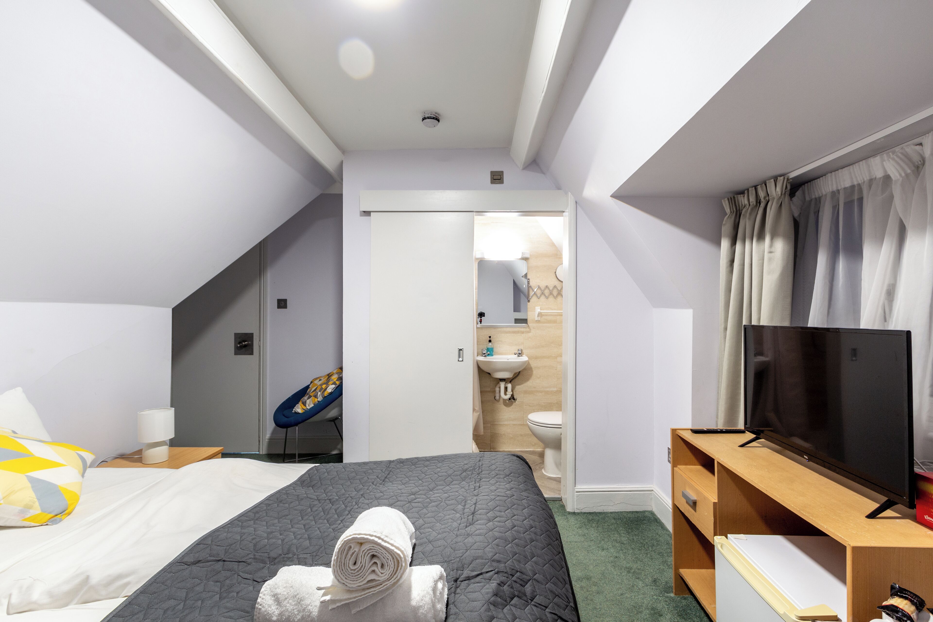 A hotel room with a bed, a TV, a desk, and a bathroom visible through an open door.