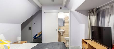 A hotel room with a bed, a TV, a desk, and a bathroom visible through an open door.