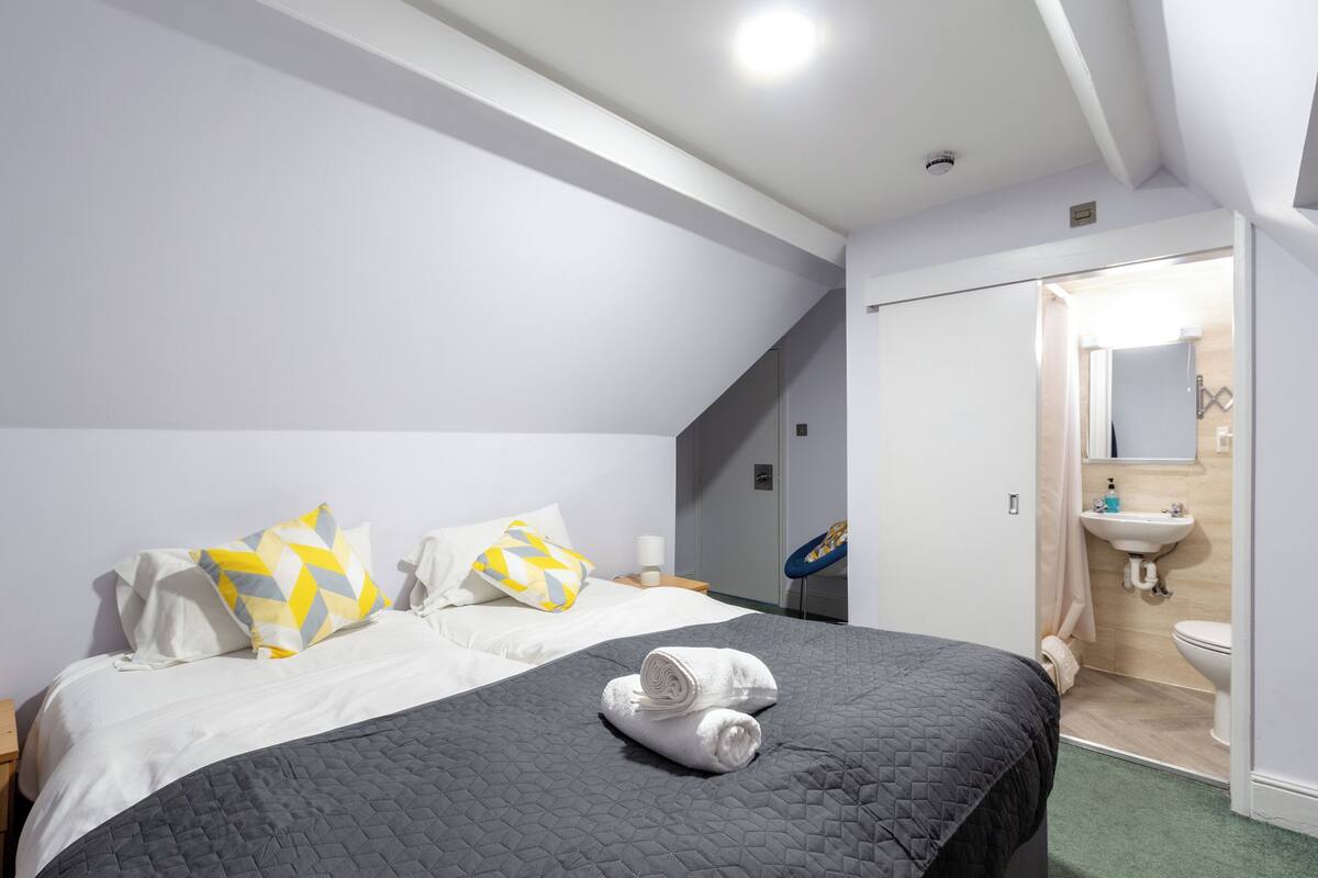 A modern hotel room with a large bed, a bathroom with a sink and toilet, and a walk-in closet.