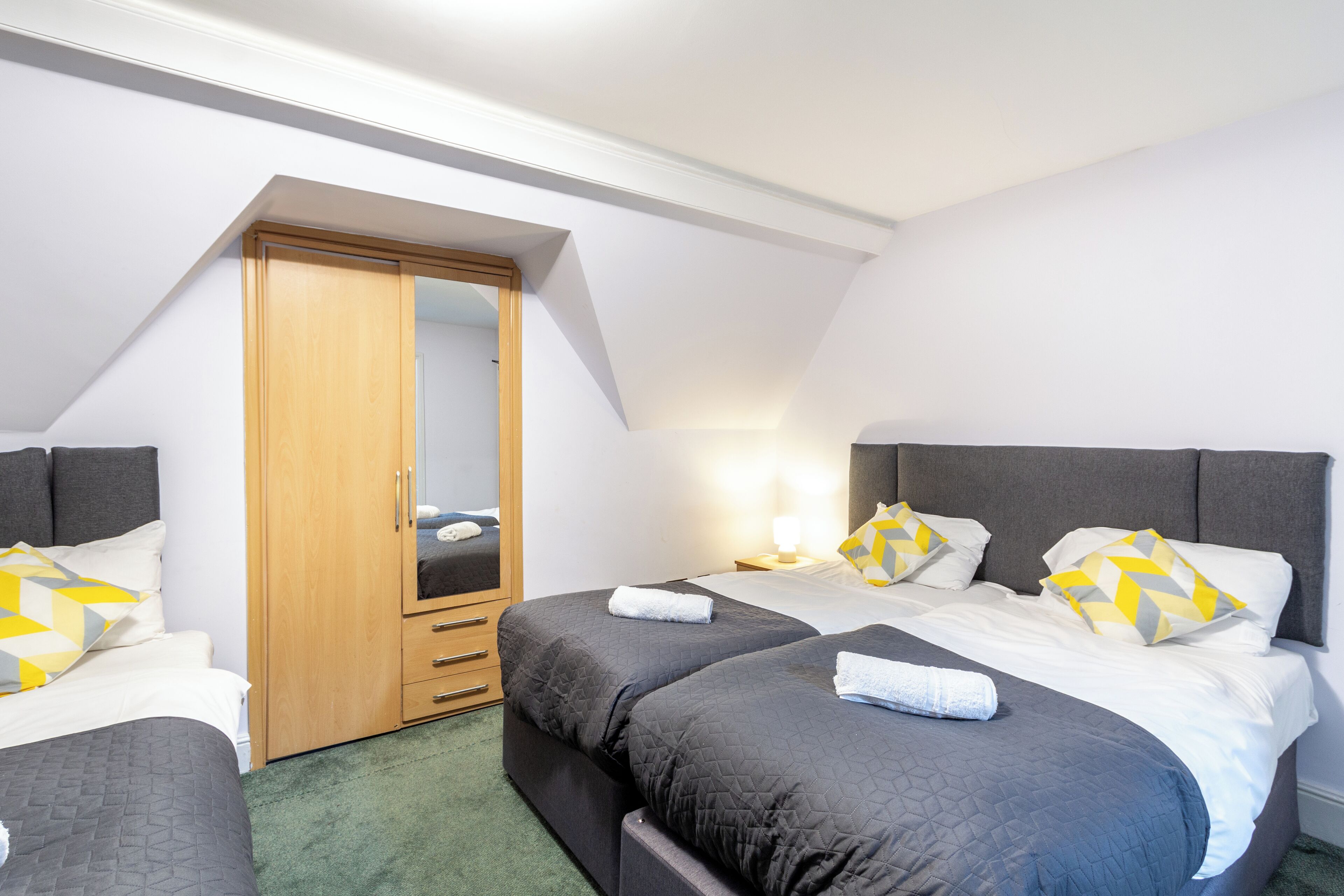 A bedroom with two beds, a wardrobe, and a mirror.