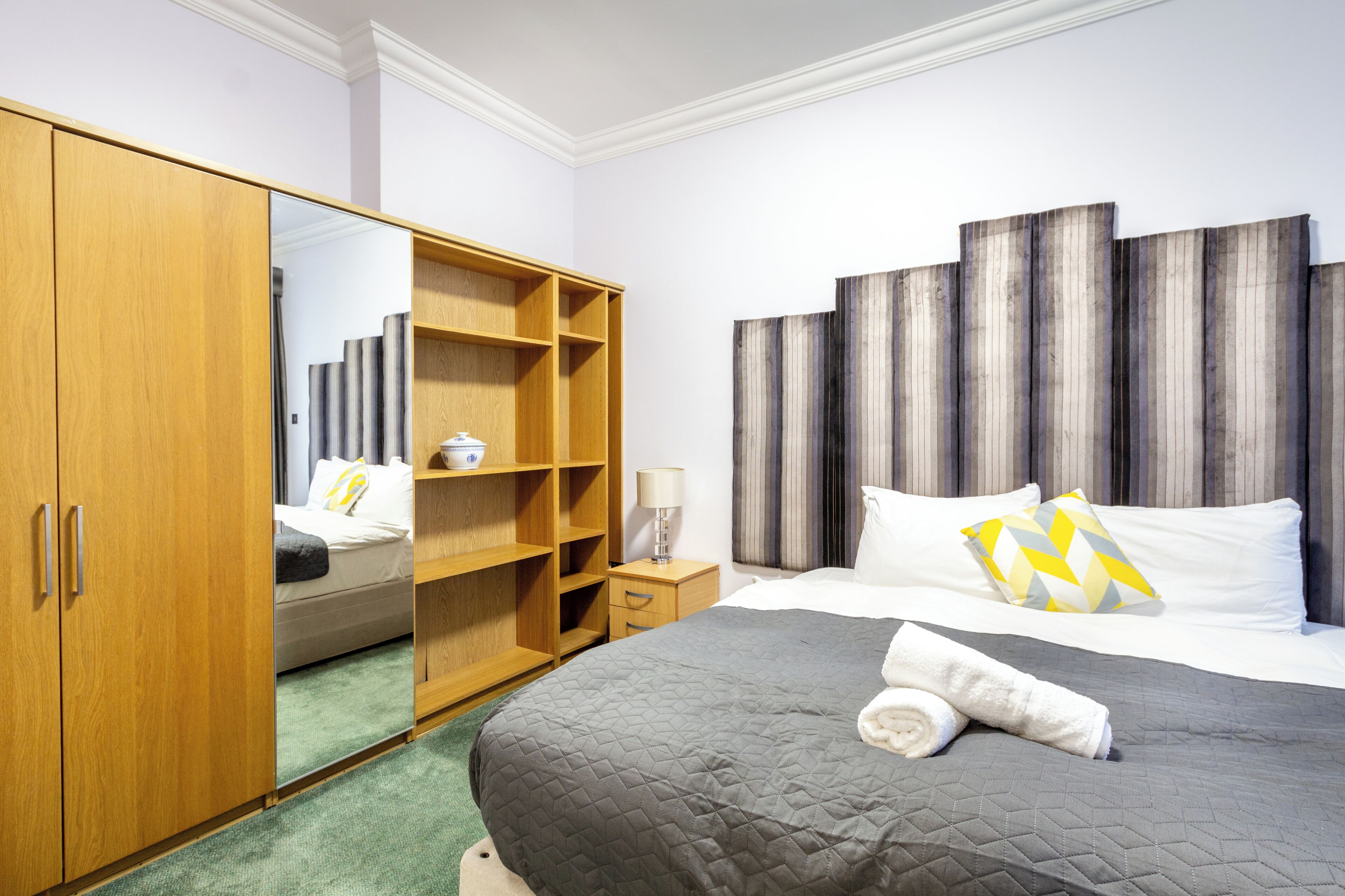 A hotel room with a bed, a wardrobe, a mirror, and a bedside table.