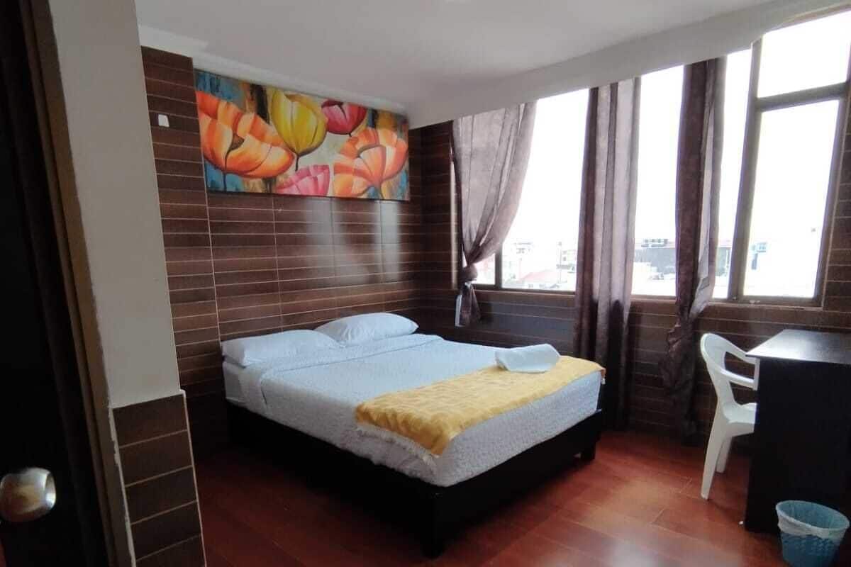A hotel room with a bed, a desk, a chair, and a colorful mural on the wall.