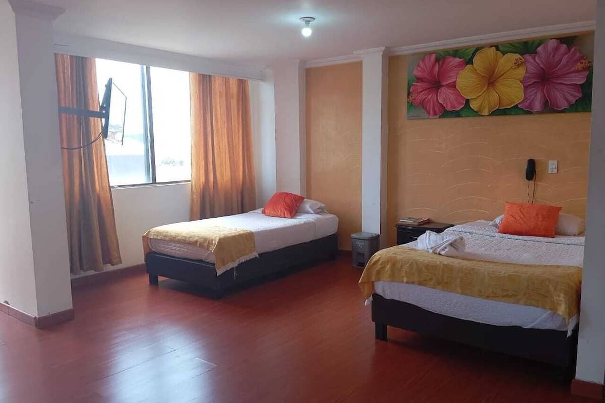 A hotel room with two single beds, wooden flooring, a large window with curtains, and a floral wall mural.