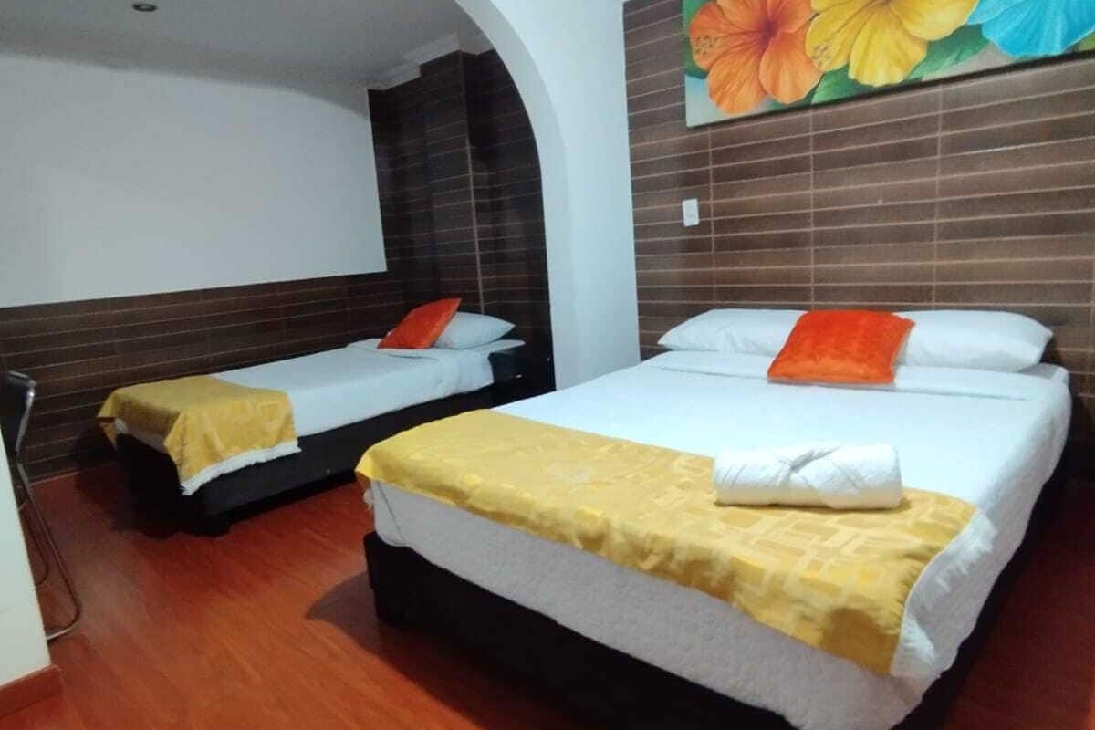A hotel room with two beds, wooden flooring, a large floral mural on the wall, and a white ceiling light.