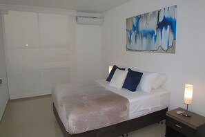 Une chambre à coucher avec un lit, une table de chevet, une lampe et un tableau abstrait.