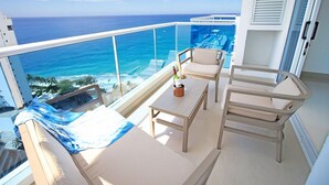 Uma varanda com vista para o oceano, um sofá, uma mesa e duas cadeiras.
